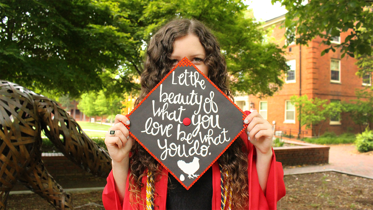 young woman holding graduation cap reading 'let the beauty of what you love be what you do' in front of her face