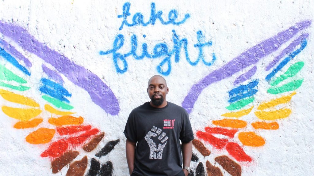 Jonathan McCorey in front of rainbow painted wings with the message Take Flight above it